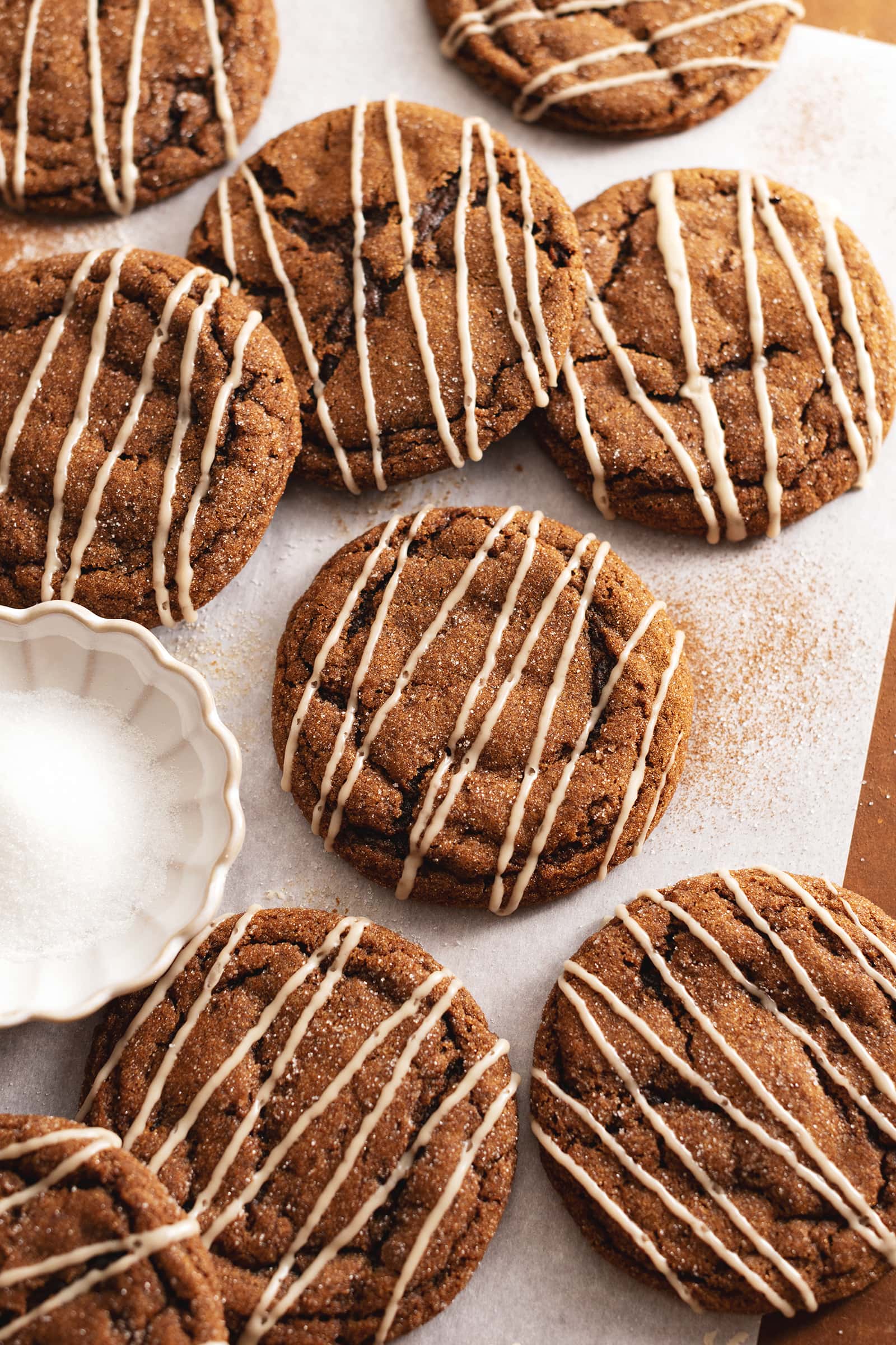 Several gingerbread latte cookies scattered on parchment paper with a small bowl of sugar.