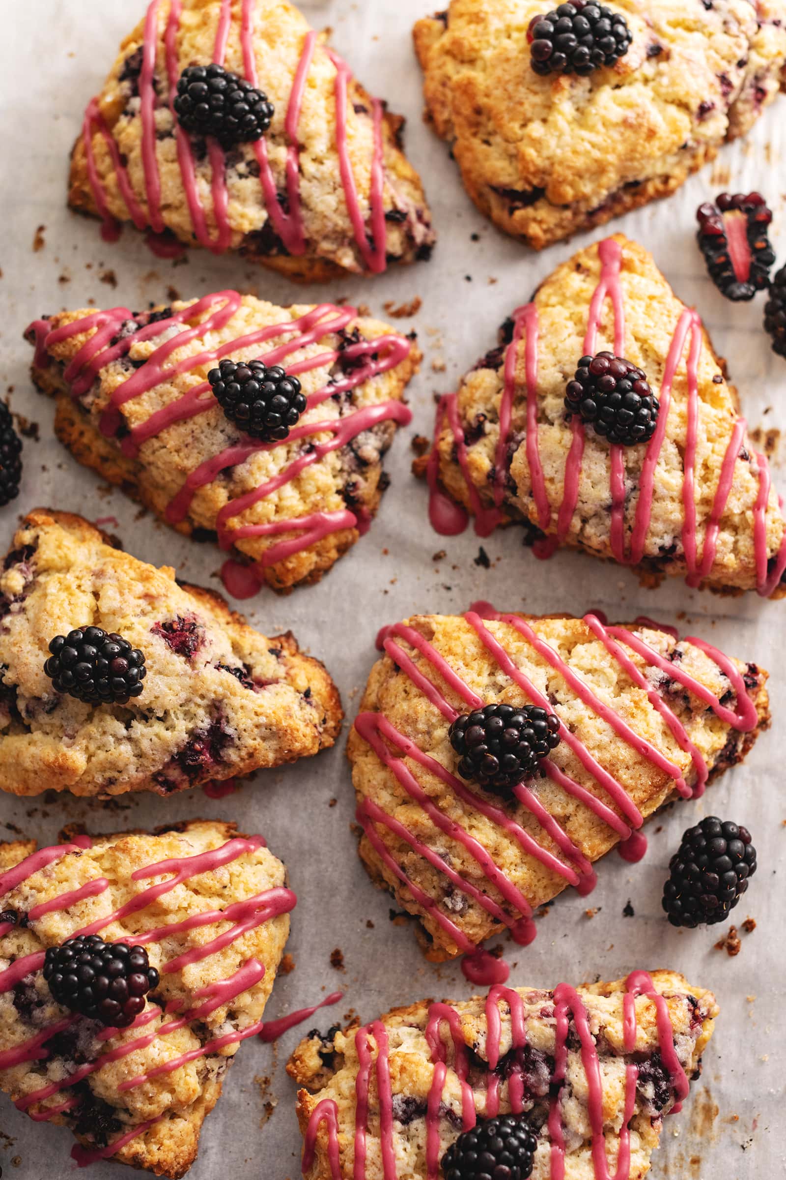 Several blackberry scones with drizzles of pink icing scattered on parchment paper.