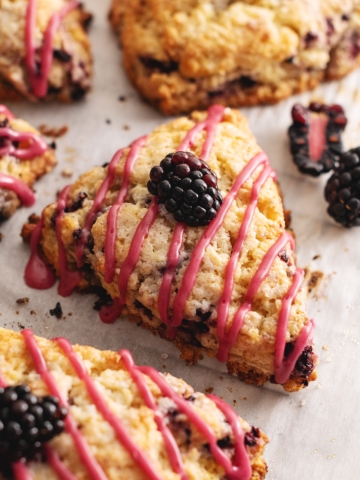 A blackberry scone with a drizzle of pink icing on parchment paper.