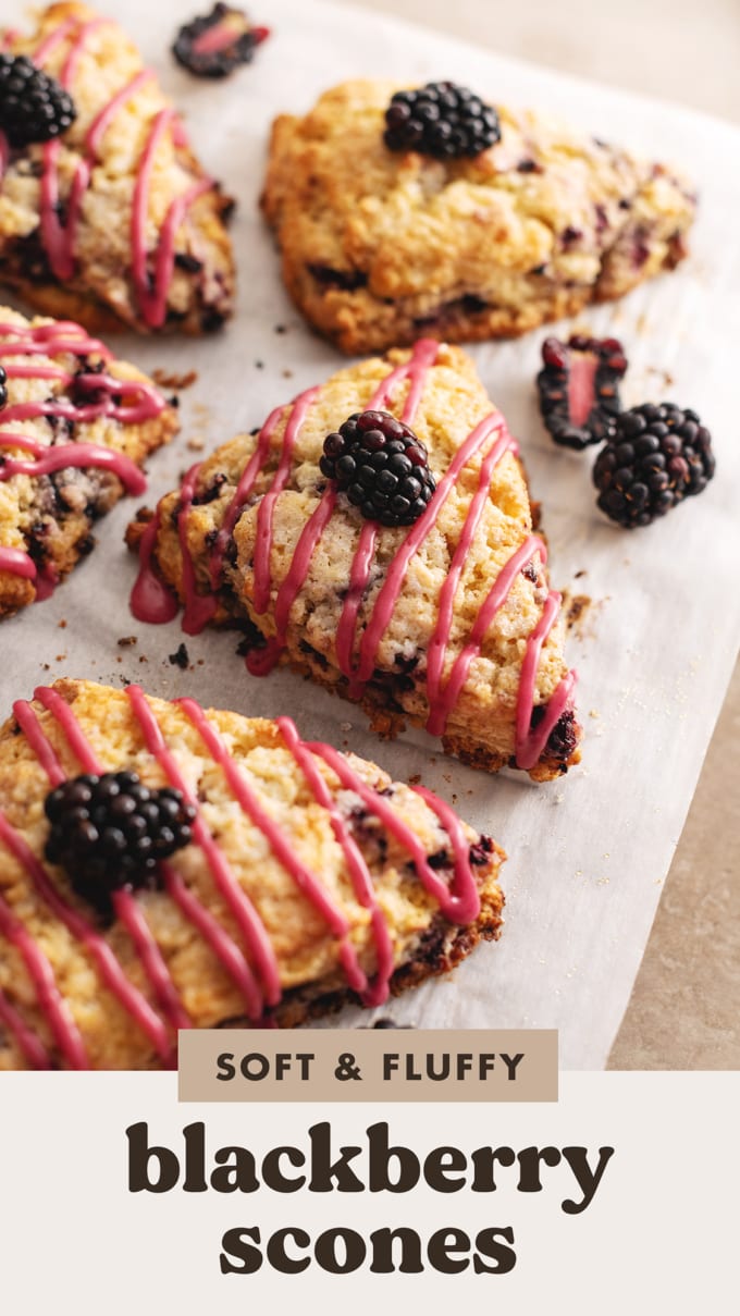 A blackberry scone with a drizzle of pink icing on parchment paper.