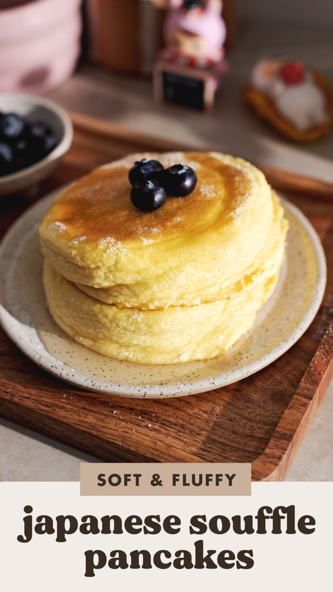 A stack of two Japanese souffle pancakes with blueberries on top on a plate and wooden tray.