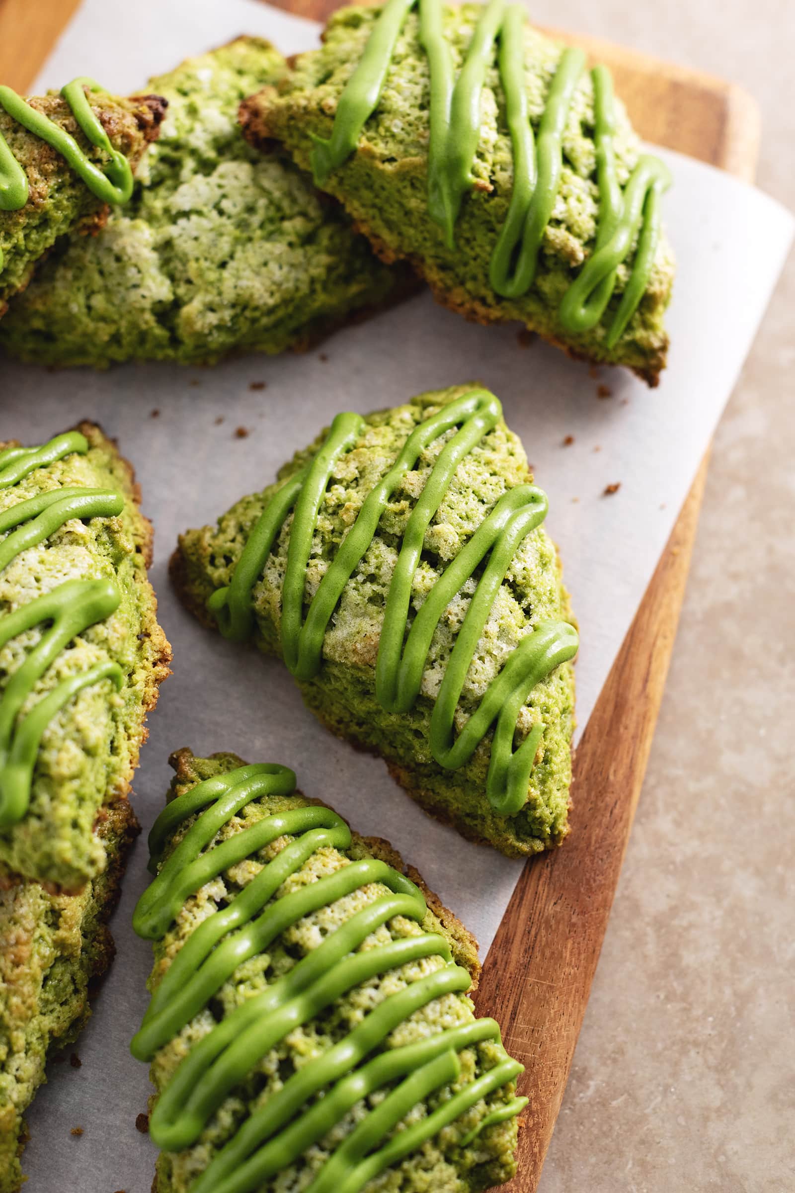 Matcha scones drizzled with matcha icing scattered on a wooden board.