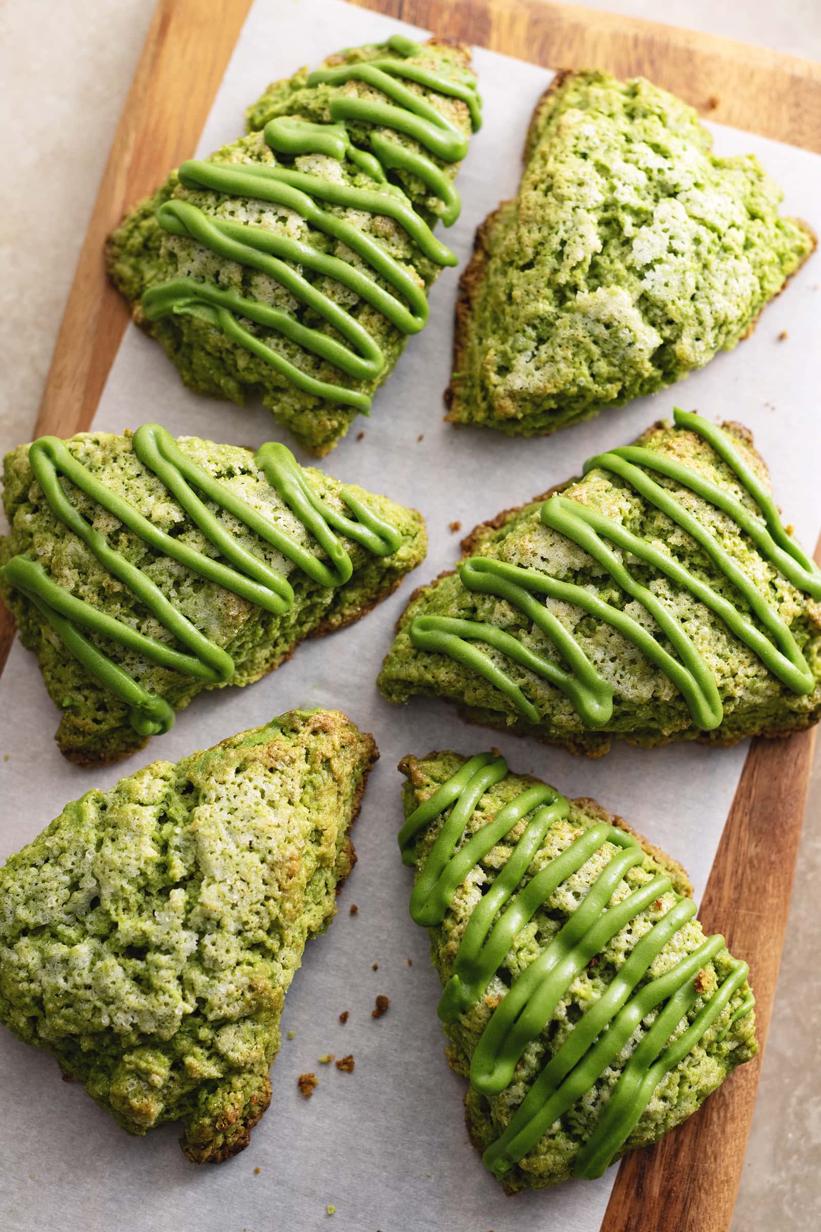 Matcha scones drizzled with matcha icing scattered on a wooden board.