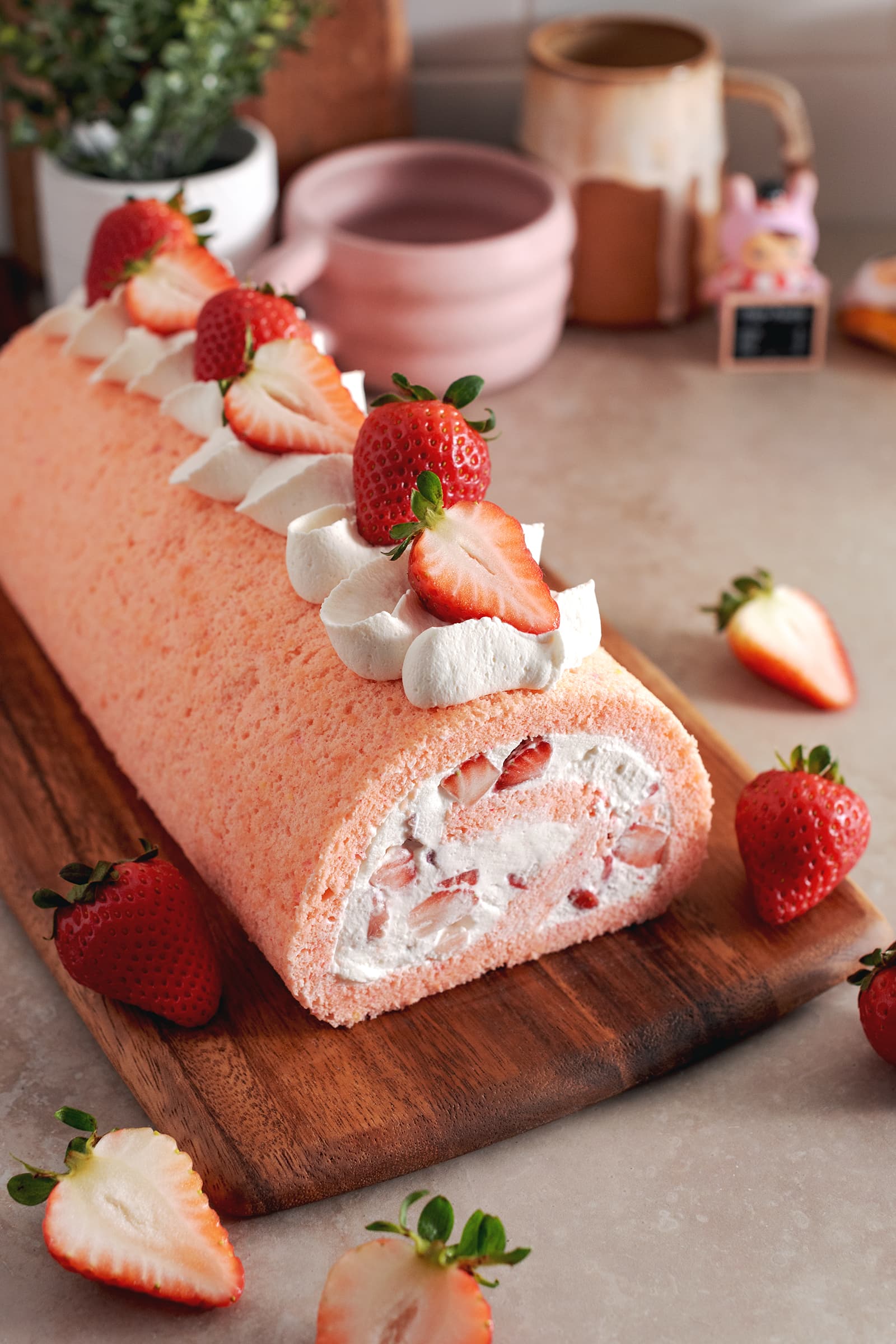 A strawberry swiss roll topped with whipped cream and strawberries before being cut on a wooden platter.