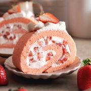 A slice of strawberry swiss roll cake rolled up with chunks of strawberries on a plate.