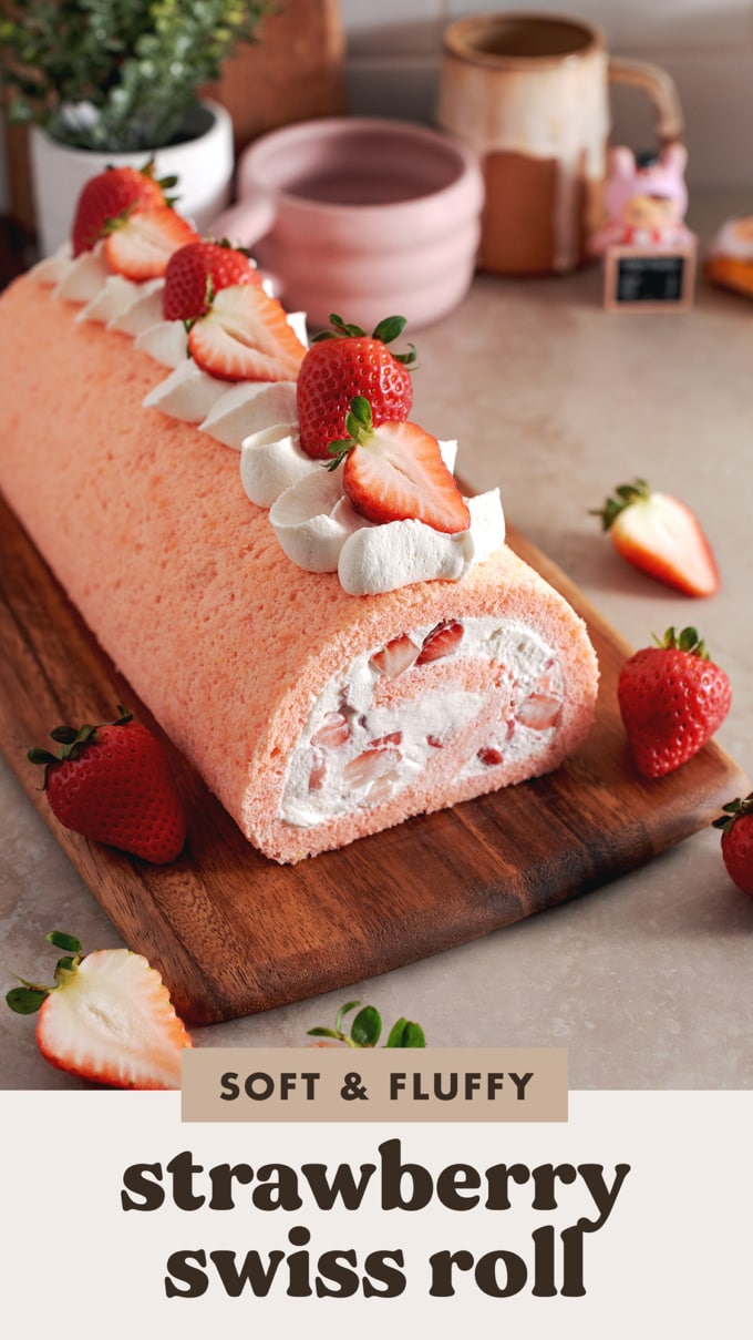 A strawberry swiss roll topped with whipped cream and strawberries before being cut on a wooden platter.