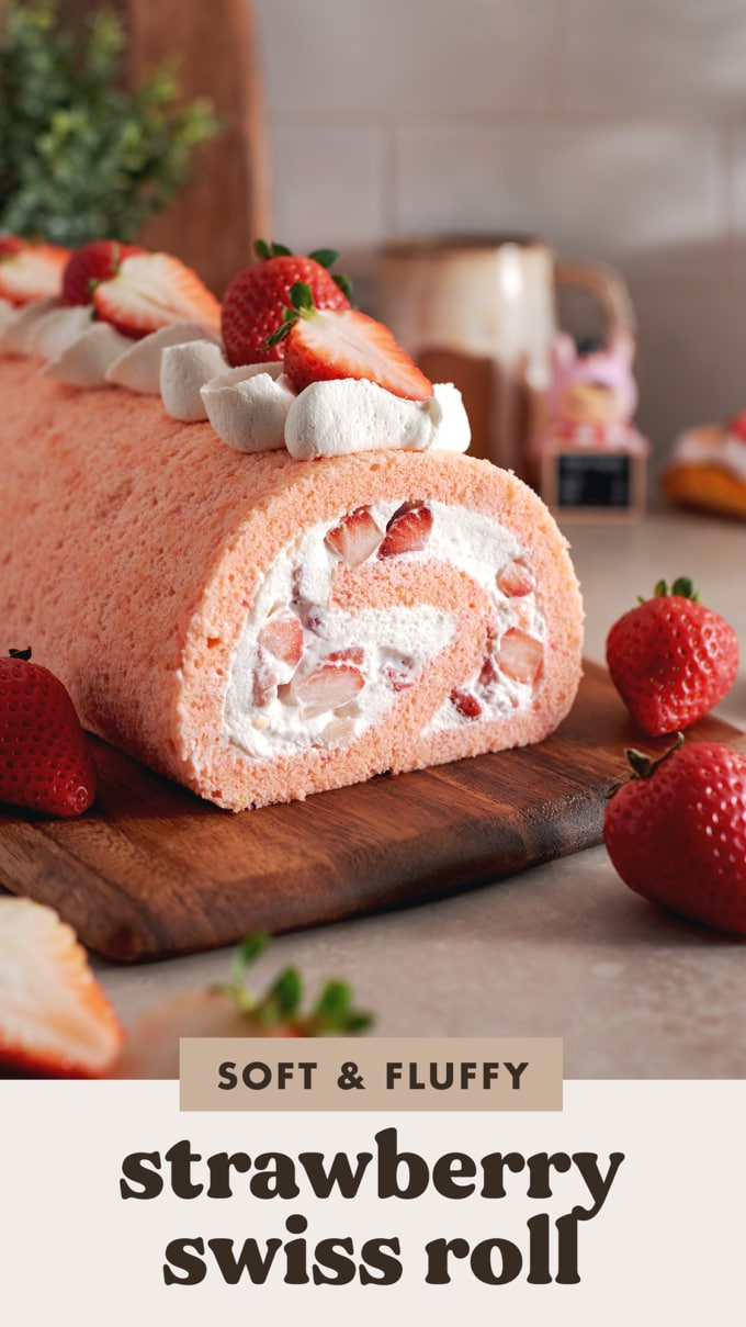 A strawberry swiss roll before being cut on a wooden platter surrounded by strawberries.