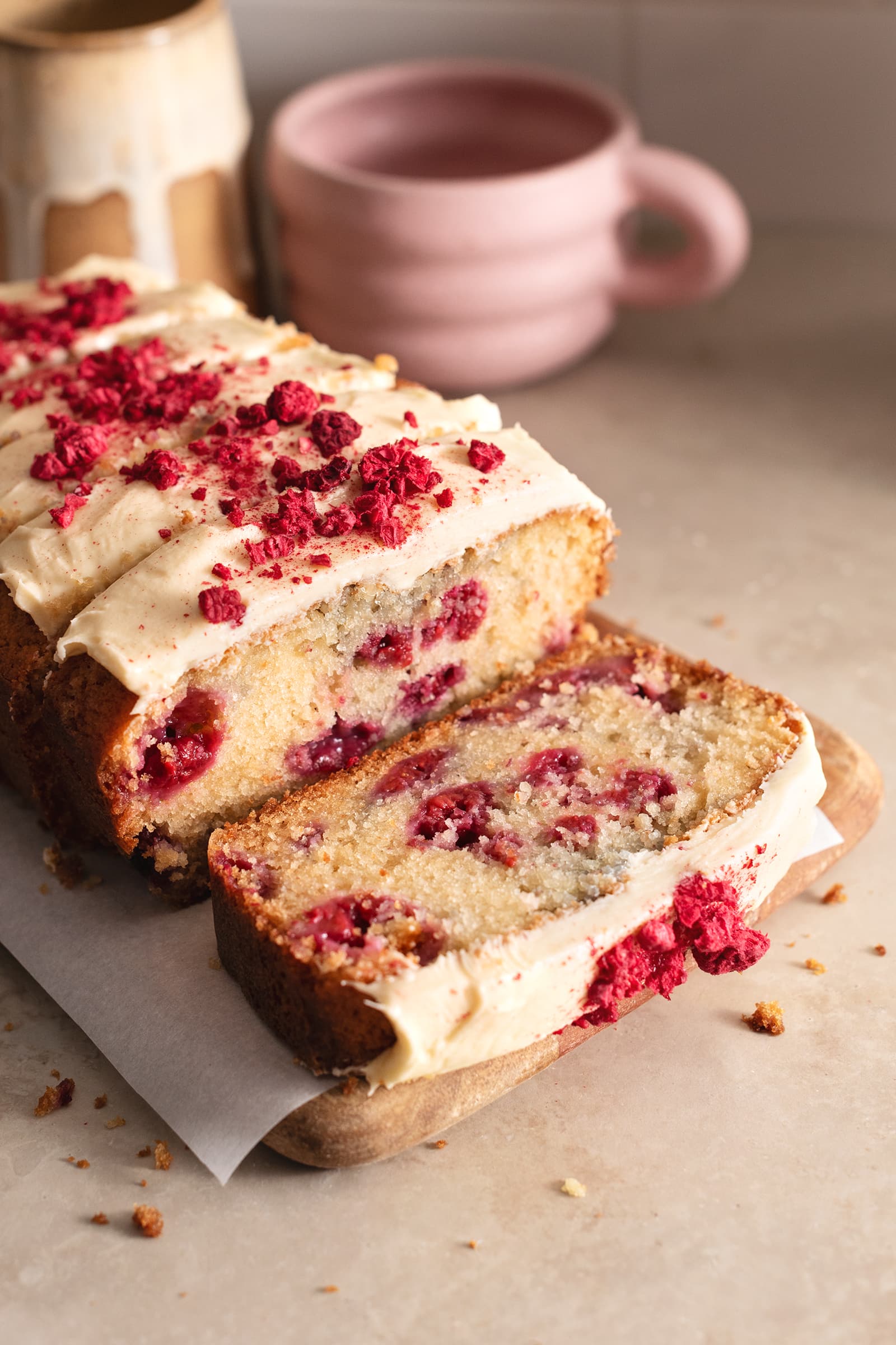 A slice of white chocolate raspberry loaf cake cut from the loaf and laying down on a wooden board.
