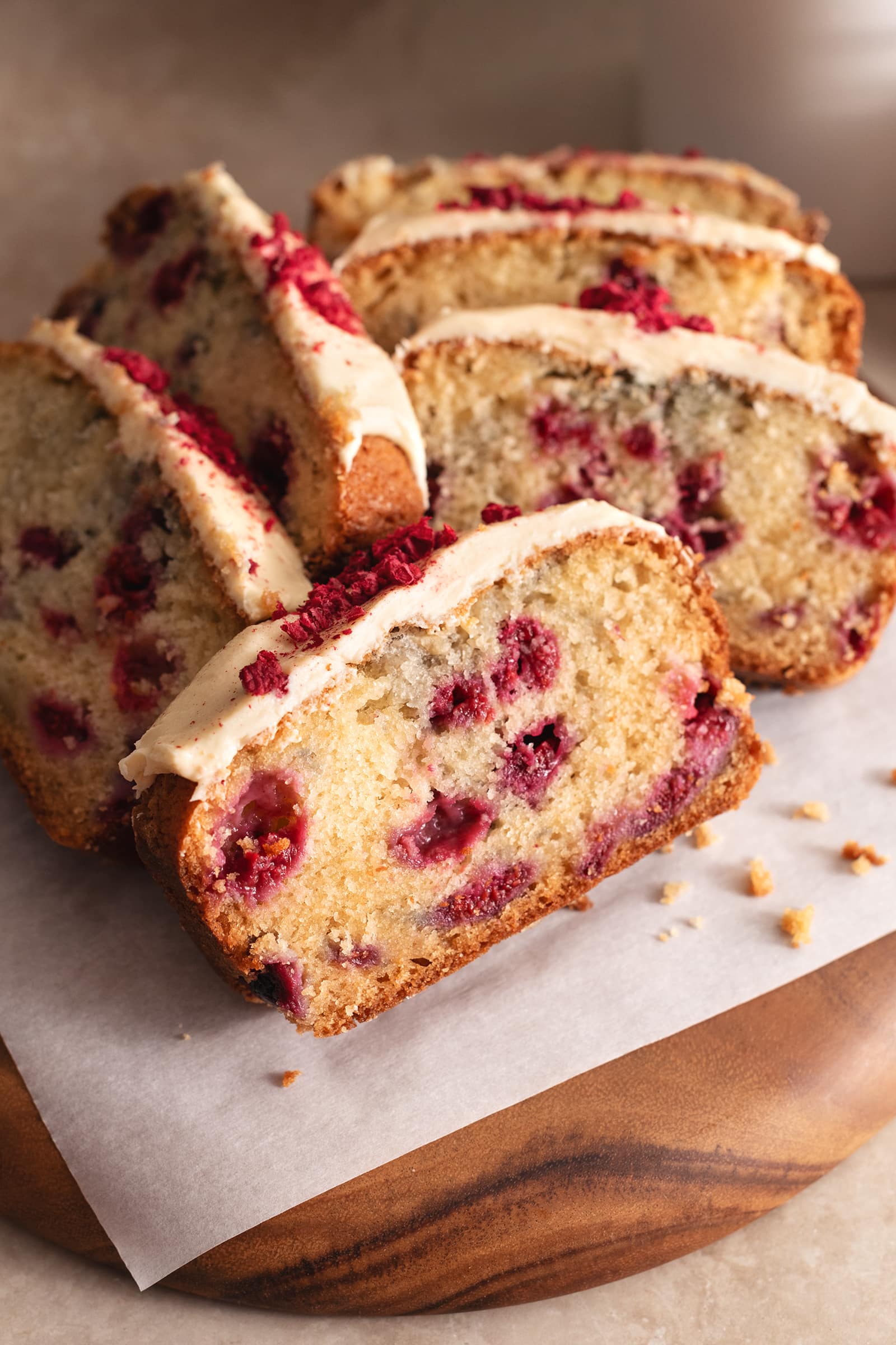 Slices of white chocolate raspberry loaf cake piled onto a wooden board.