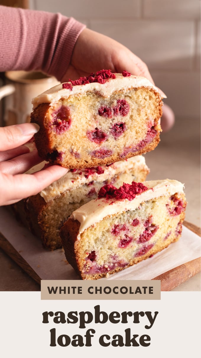 Hands holding up a slice of white chocolate raspberry loaf cake above the other slices.