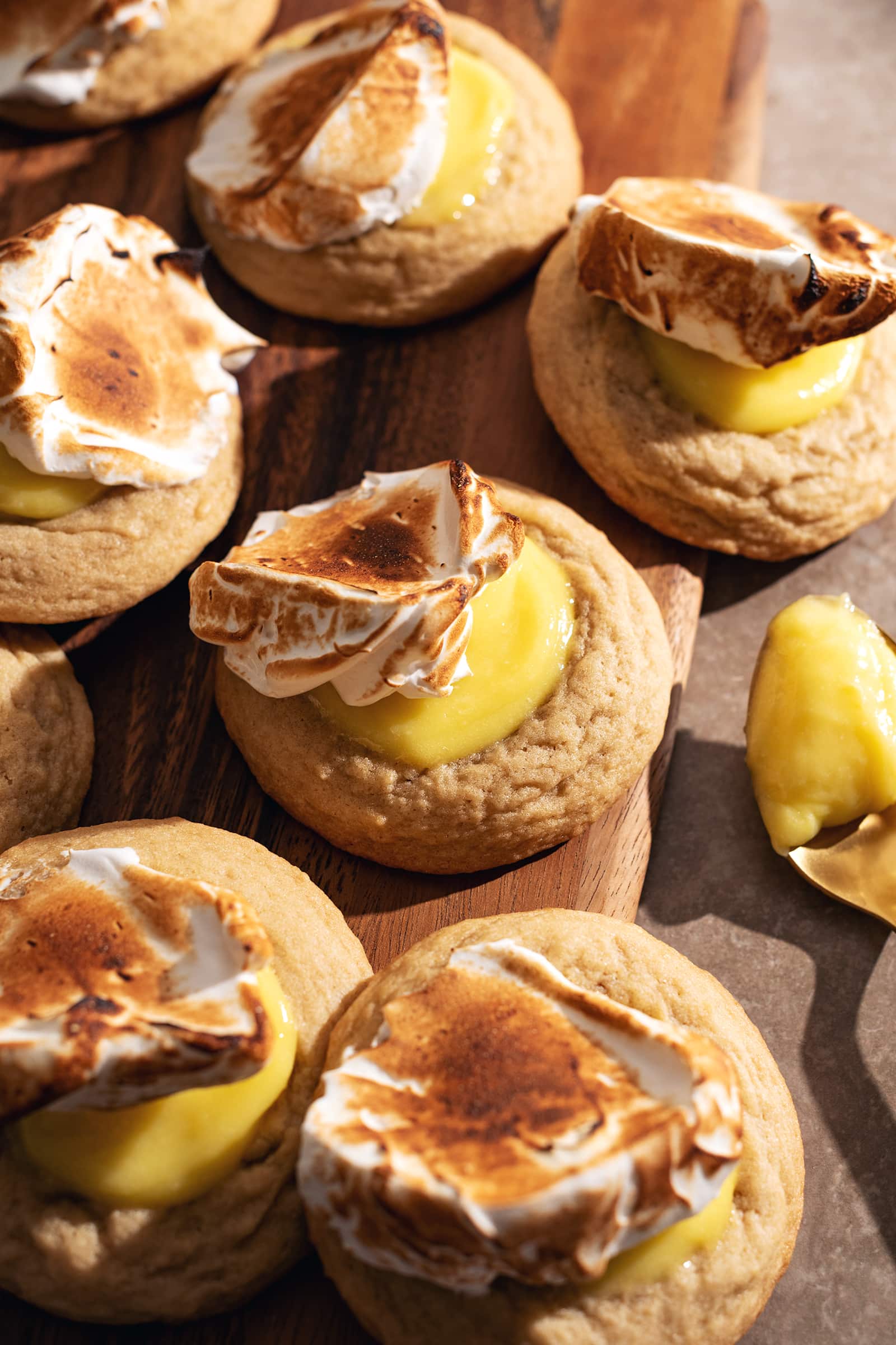 Several lemon meringue cookies topped with dollops of toasted meringue scattered on a wooden board.