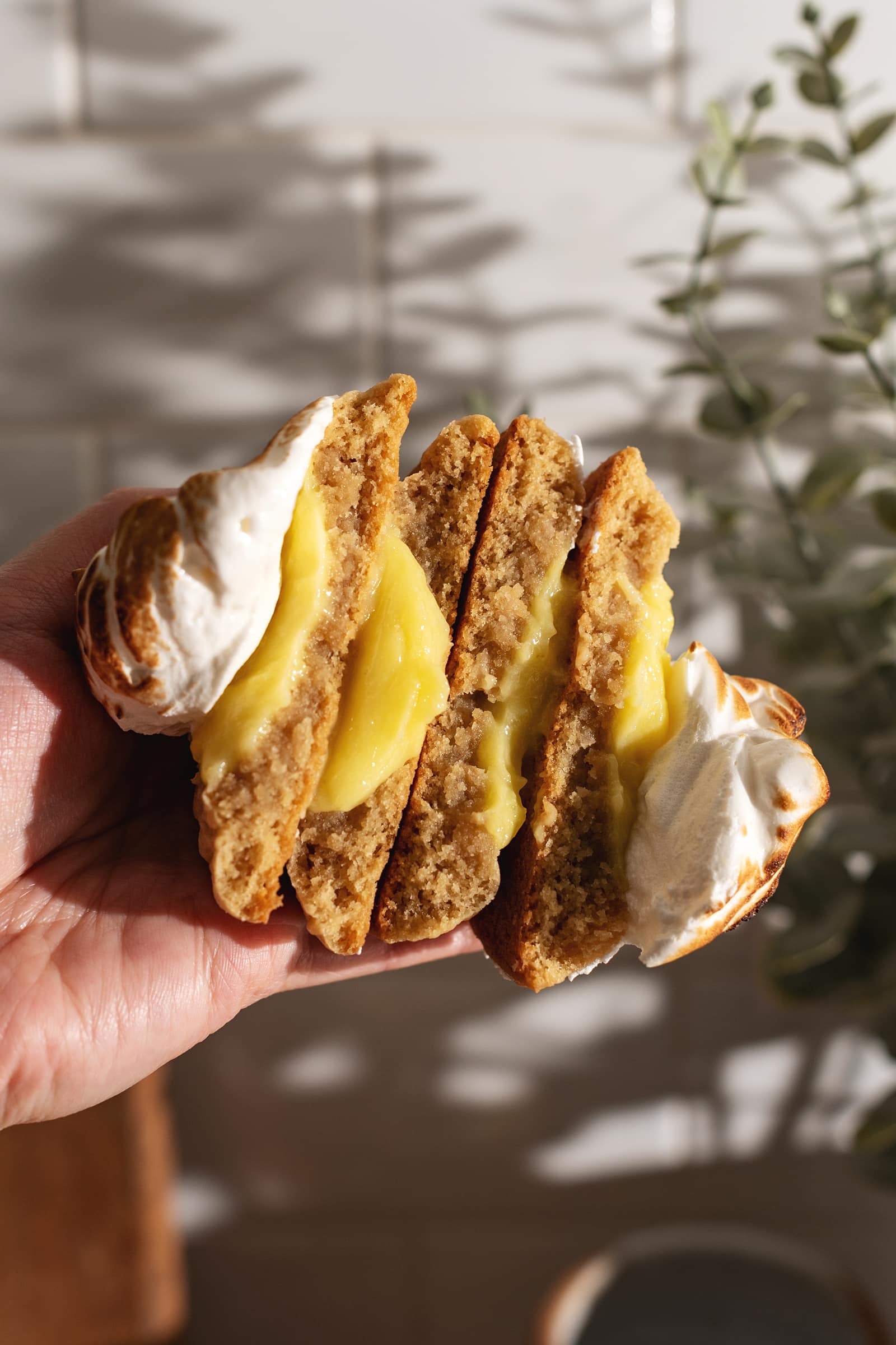 A hand holding a stack of four cookie halves to show the texture and lemon curd inside.