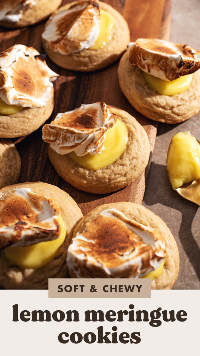 Several lemon meringue cookies topped with dollops of toasted meringue scattered on a wooden board.