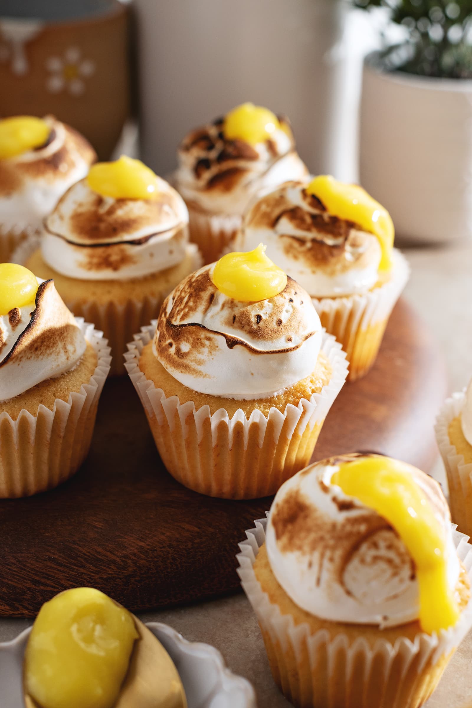 Close up of a lemon meringue cupcake on a wooden platter surrounded by more cupcakes.