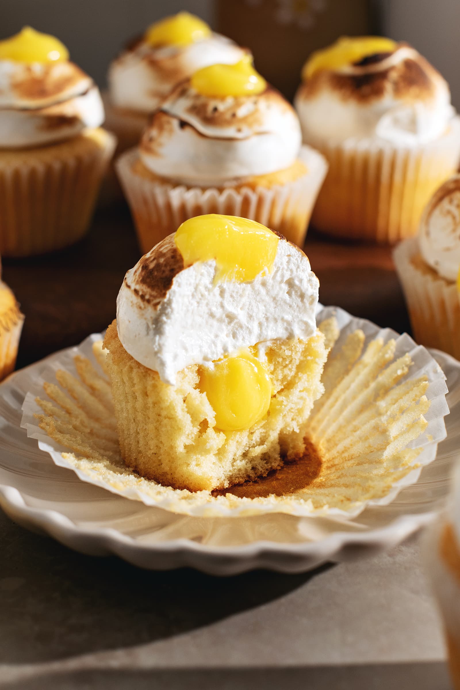 A lemon meringue cupcake cut in half to show the cross section and the lemon curd filling inside.