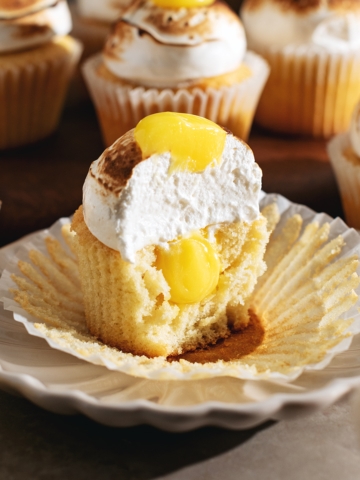 A lemon meringue cupcake cut in half to show the cross section and the lemon curd filling inside.
