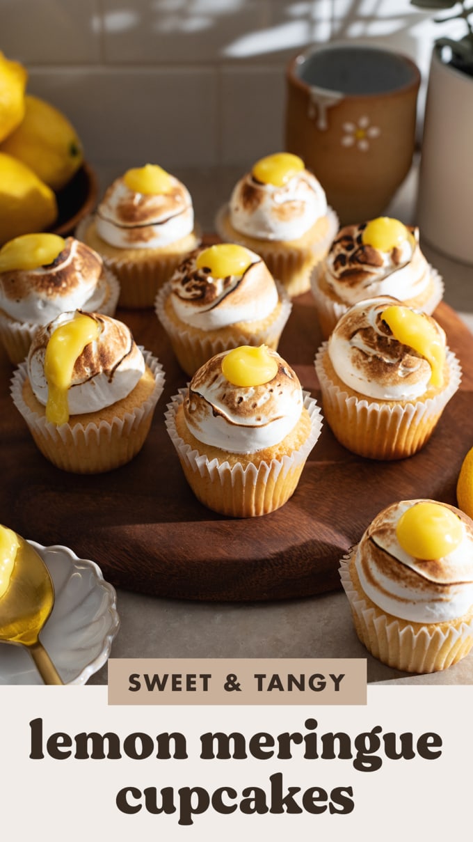 Several lemon meringue cupcakes lined up on a wooden tray.