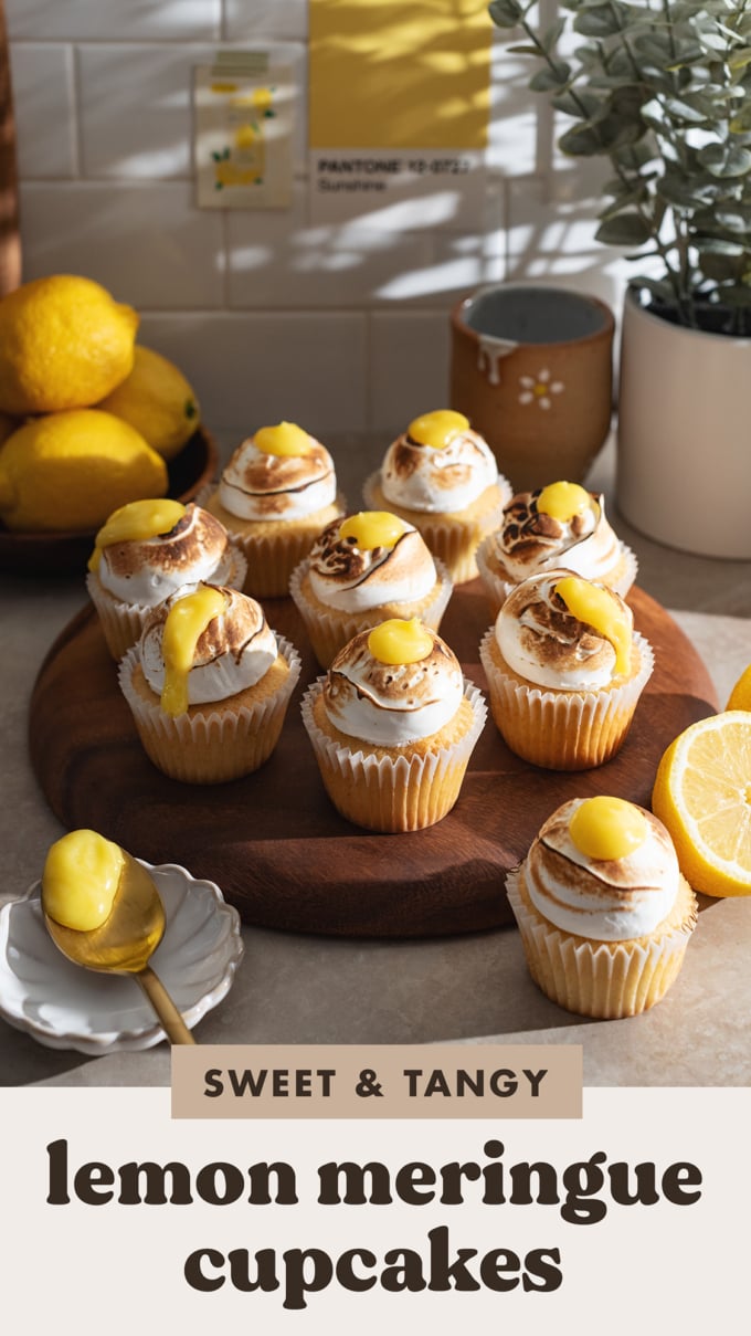 Several lemon meringue cupcakes lined up on a wooden tray on a kitchen counter.