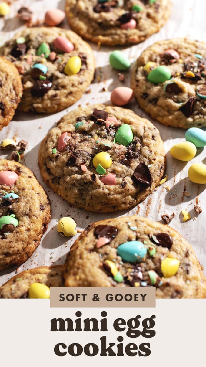 Mini egg cookies on parchment paper studded with pastel mini eggs and chocolate chunks.