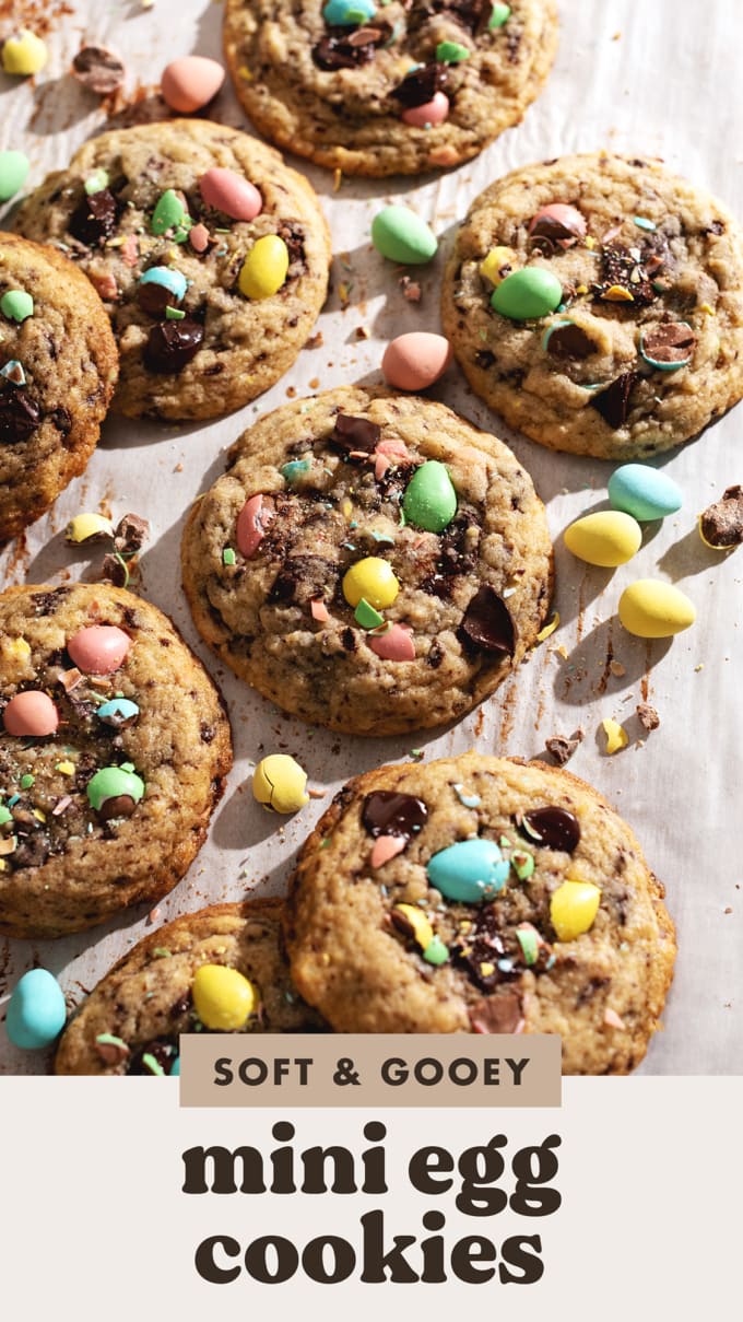 Mini egg cookies scattered on parchment paper with mini egg chocolates surrounding them.