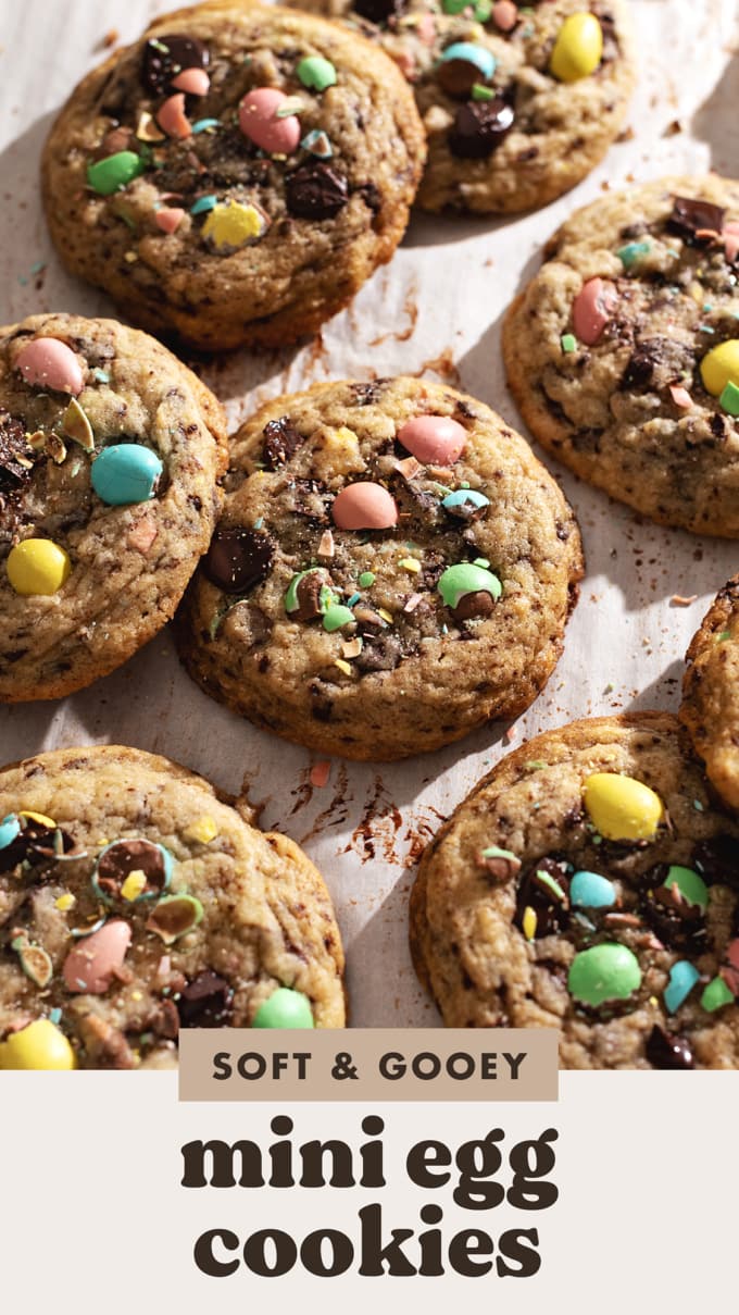 Mini egg cookies scattered on parchment paper topped with pastel mini egg chocolates.