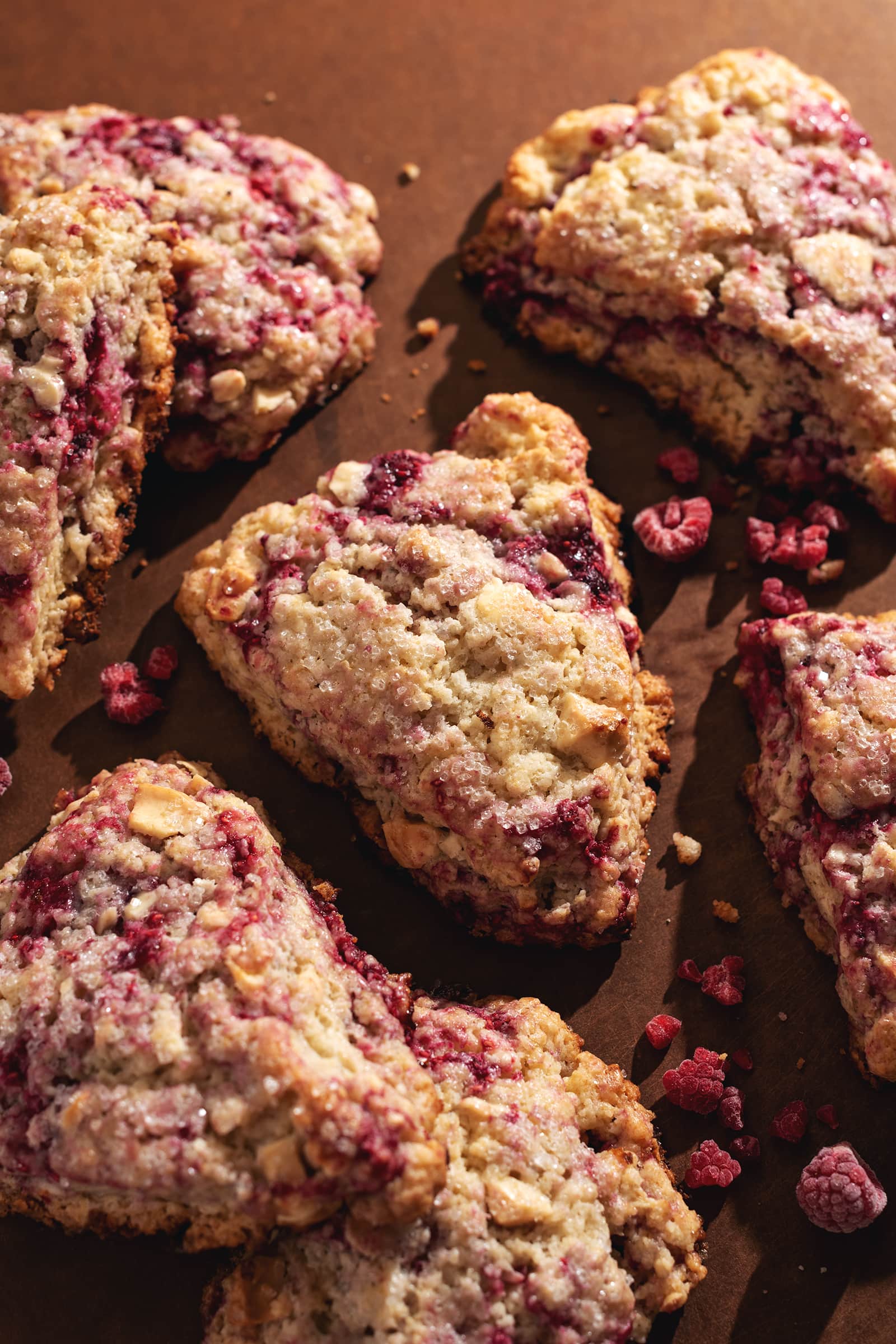 White chocolate raspberry scones scattered on a brown surface.