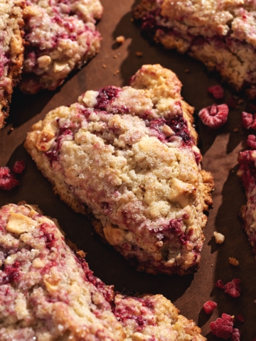 White chocolate raspberry scones scattered on a brown surface.