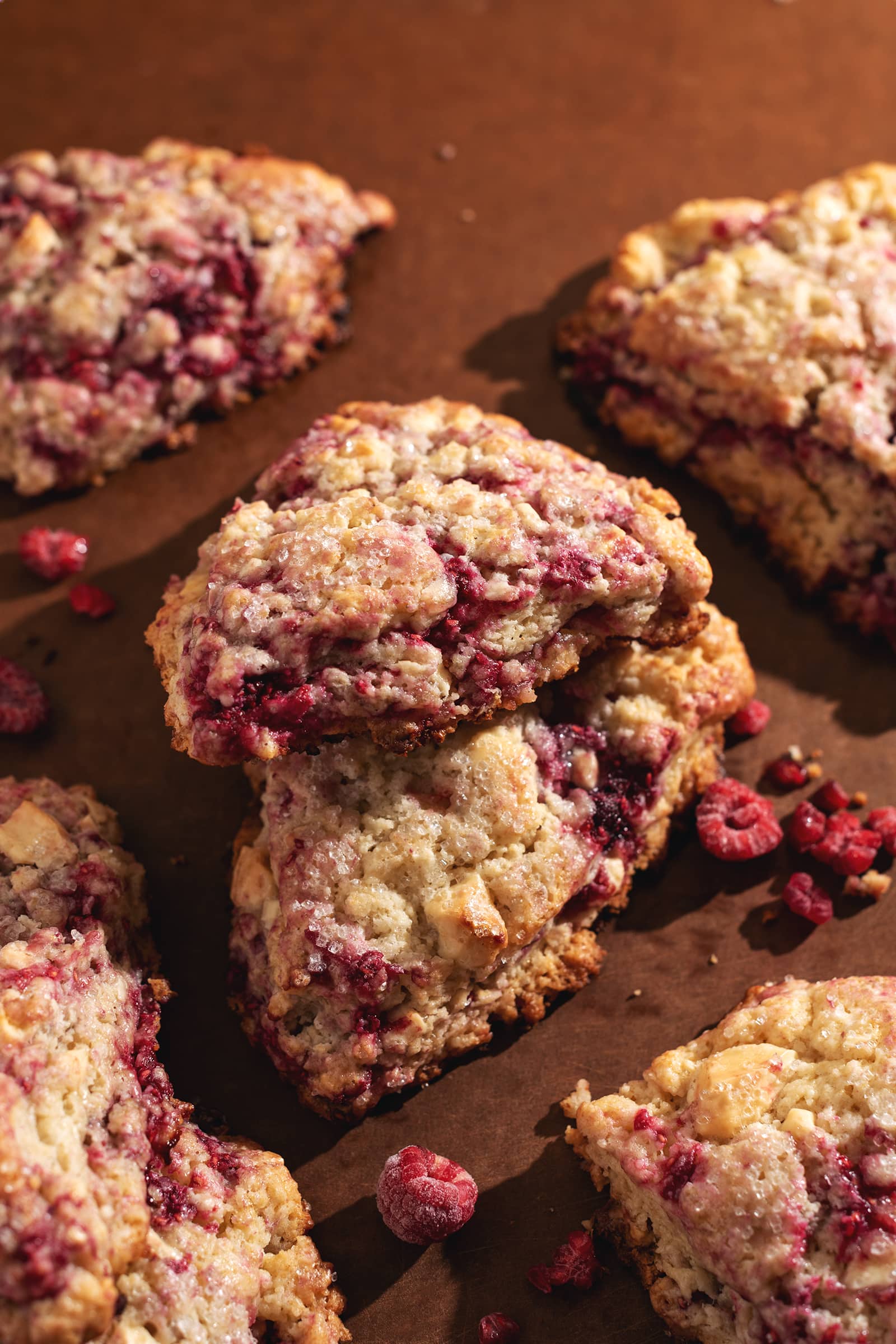 A white chocolate raspberry scone propped up on top of another scone to show the raspberry bits peeking through the dough.