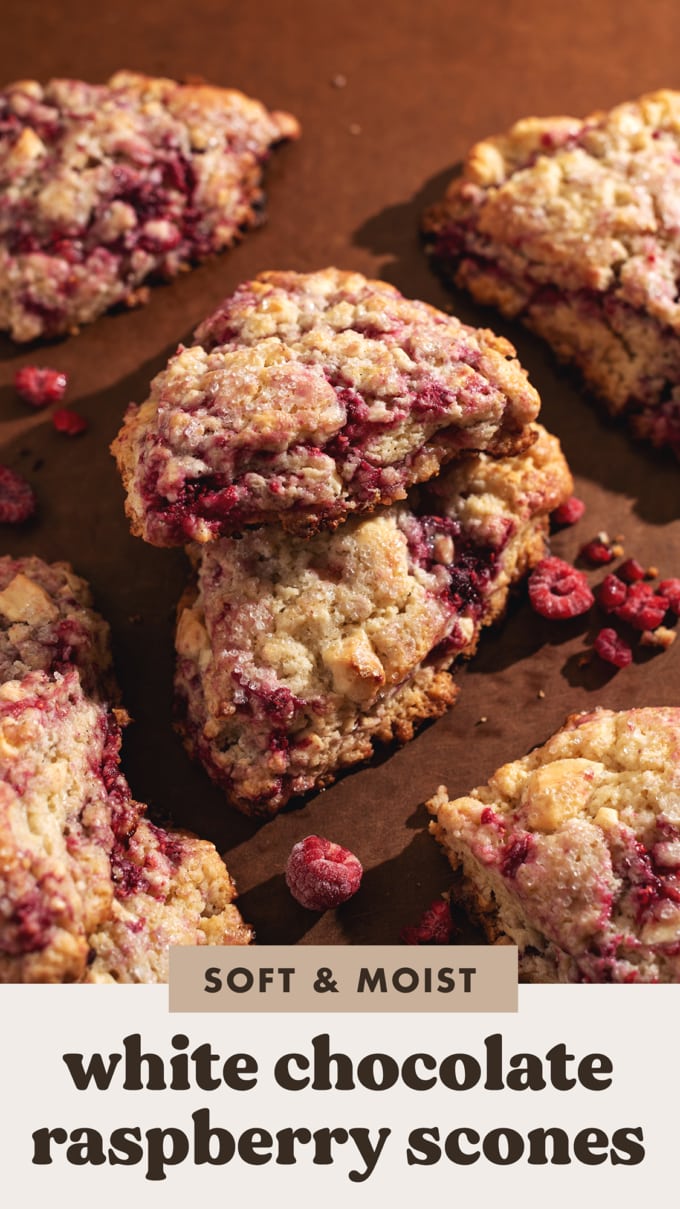 A white chocolate raspberry scone propped up on top of another scone to show the raspberry bits peeking through the dough.