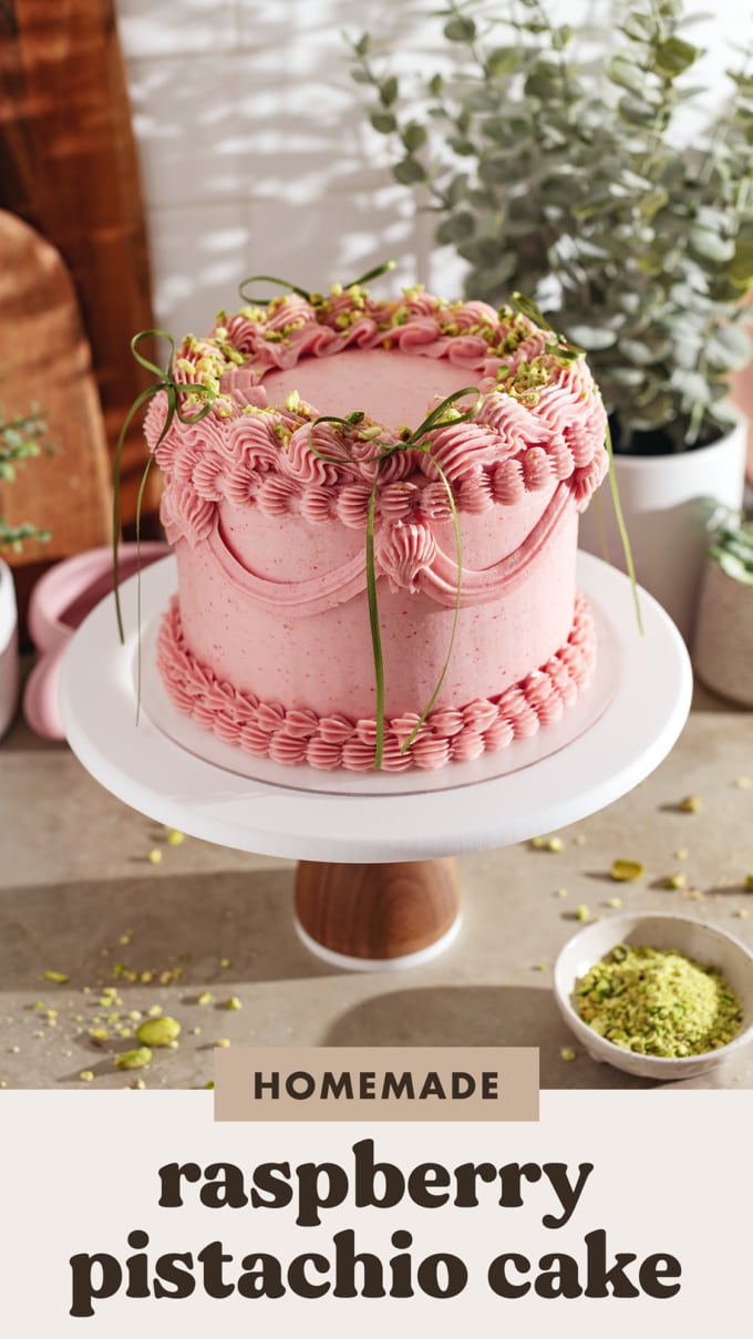 A raspberry pistachio cake on a cake stand covered with an elegant buttercream design and decorated with ribbon bows.