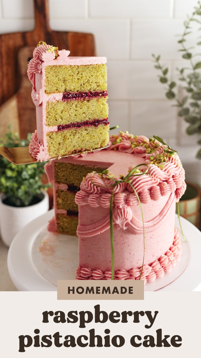A slice of raspberry pistachio cake lifted above the rest of the cake with a cake server.