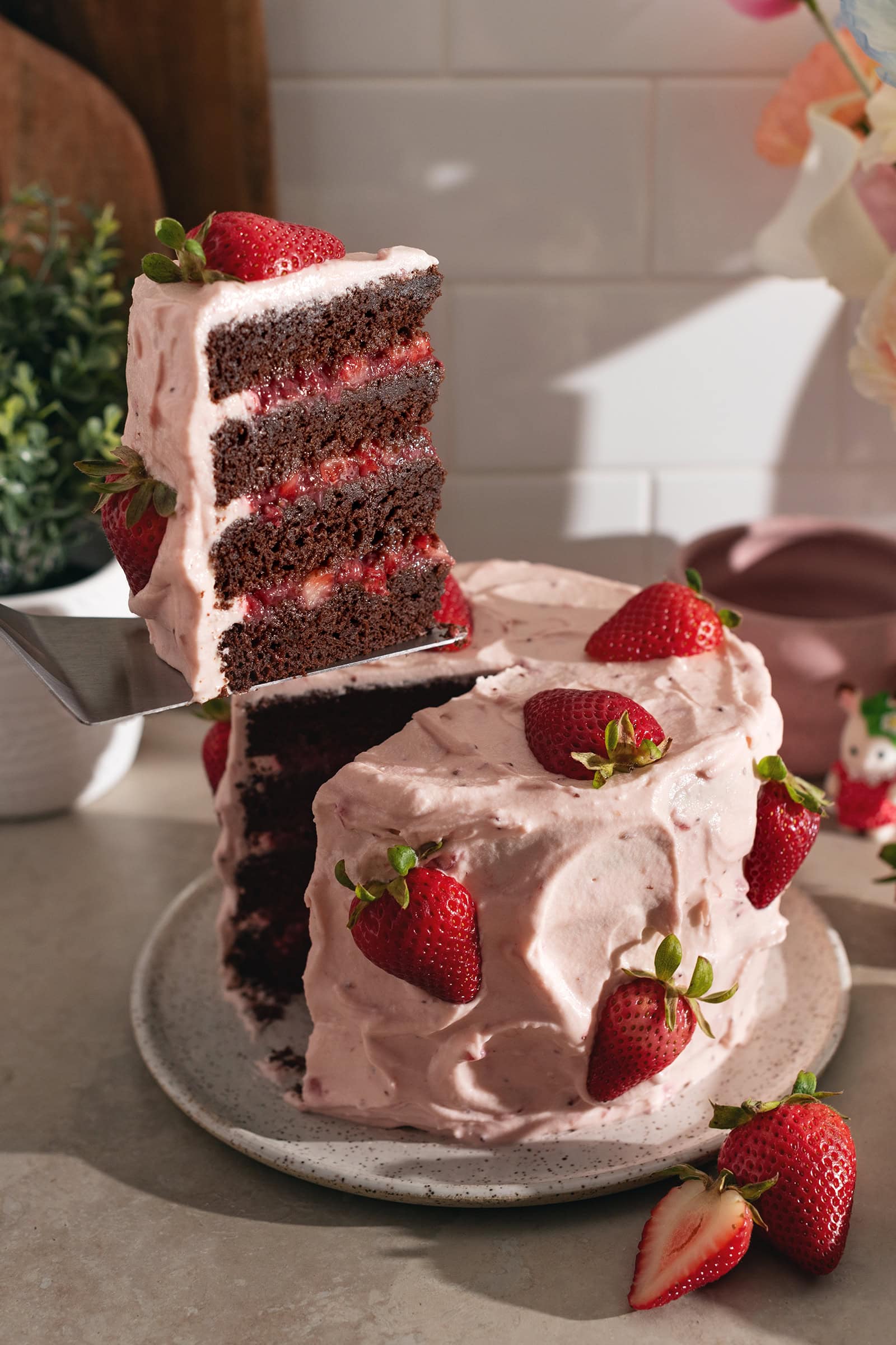 Lifting a slice of strawberry chocolate cake from the rest of the cake with a cake server.