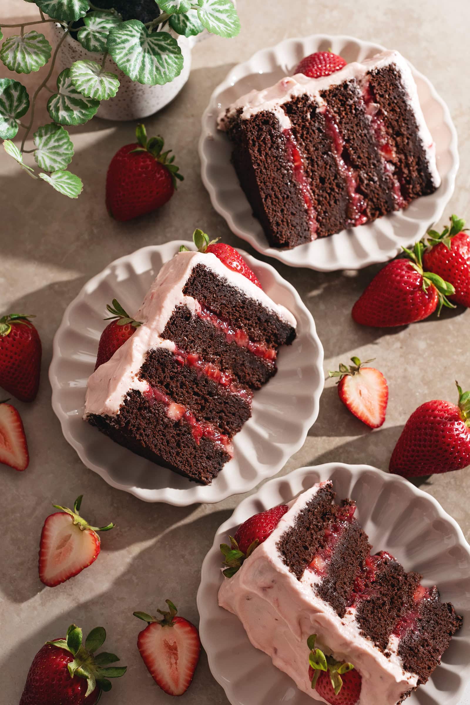Three slices of chocolate strawberry cake on plates surrounded by strawberries.