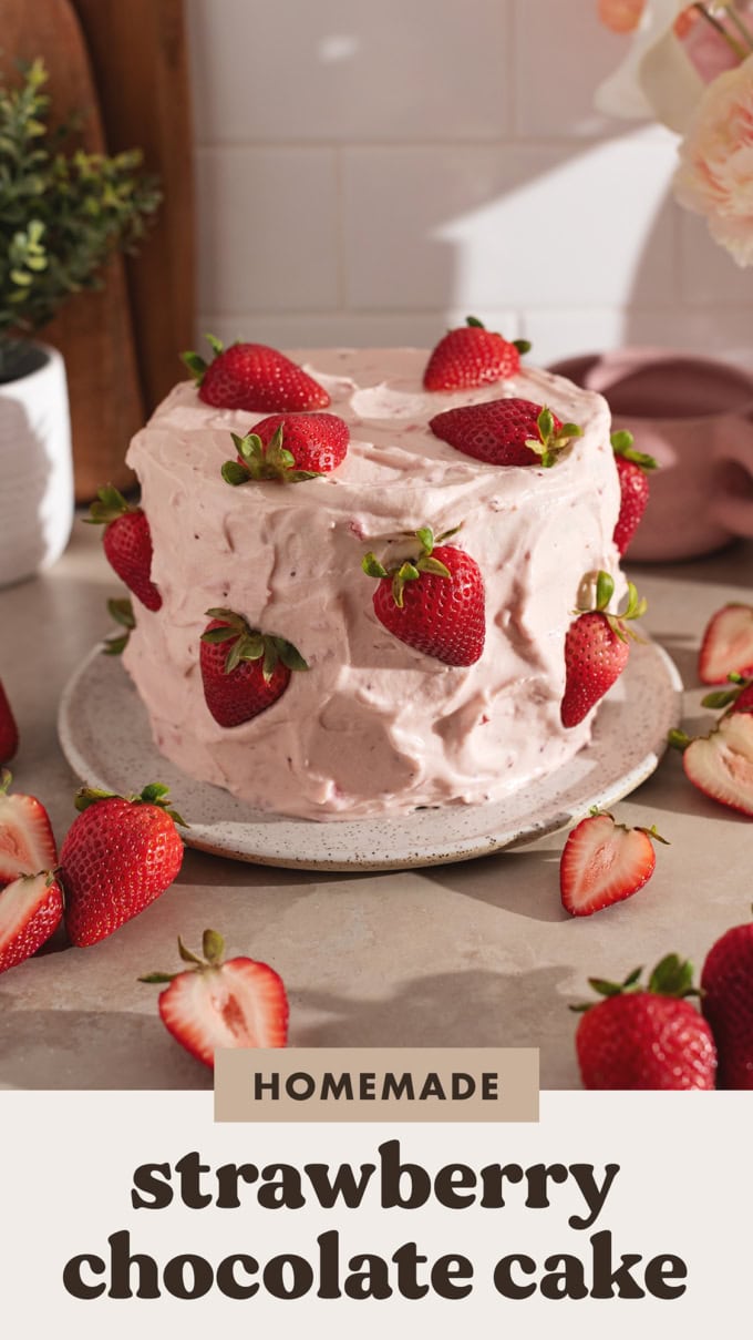 A cake covered in strawberry frosting and fresh strawberries on a plate surrounded by more strawberries.