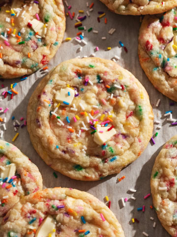 Several birthday cake cookies and rainbow sprinkles scattered on parchment paper.