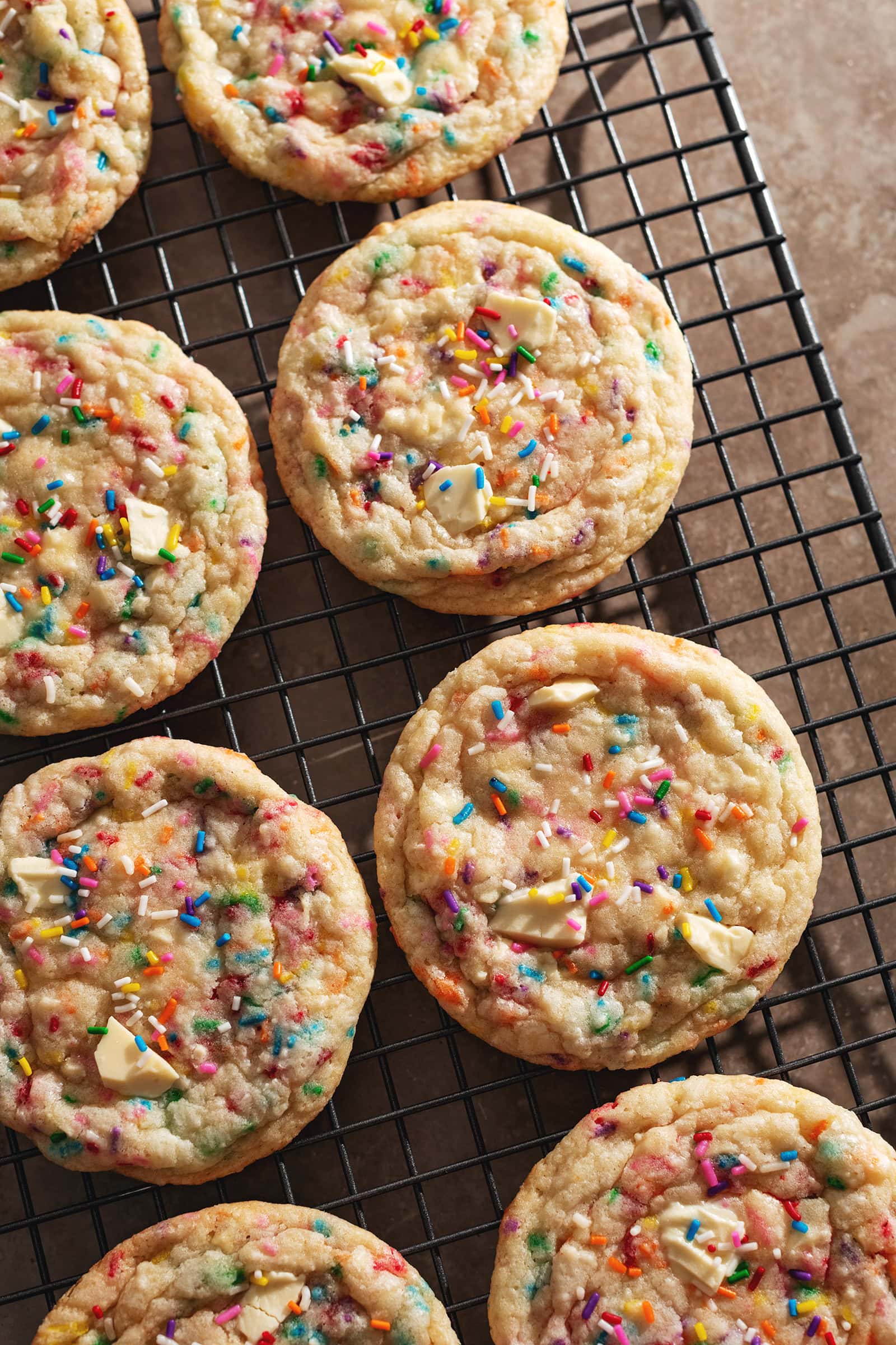 Several birthday cake cookies lined up on a wire rack.