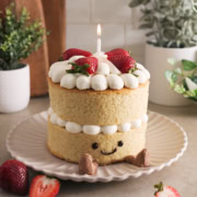 Jellycat birthday cake with a lit candle sitting on a plate.