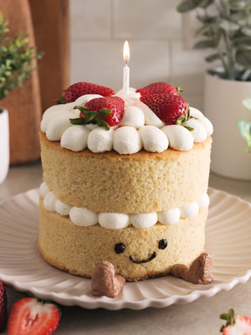 Jellycat birthday cake with a lit candle sitting on a plate.