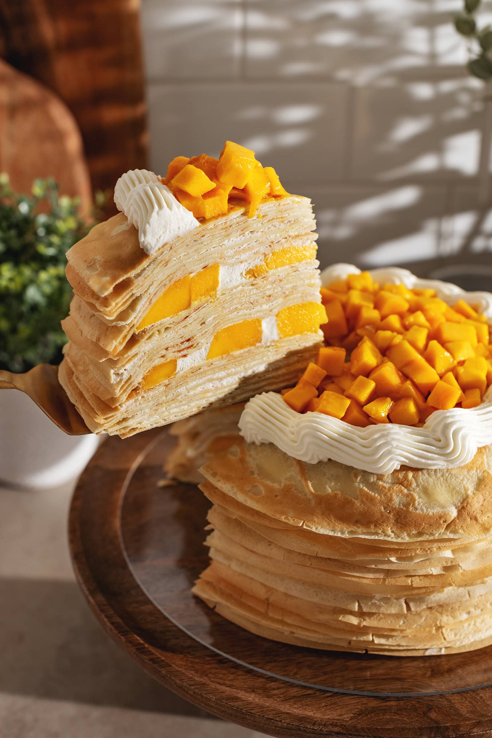 A slice of mango crepe cake lifted from the rest of the cake with a cake server.