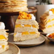 A slice of mango crepe cake on a plate showing the layers of crepes and mangoes.
