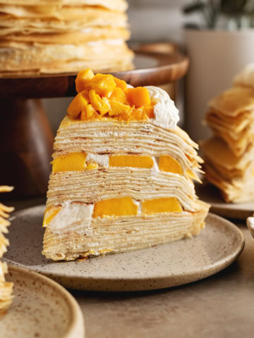 A slice of mango crepe cake on a plate showing the layers of crepes and mangoes.