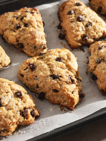Several banana chocolate chip scones lined up on a baking tray.