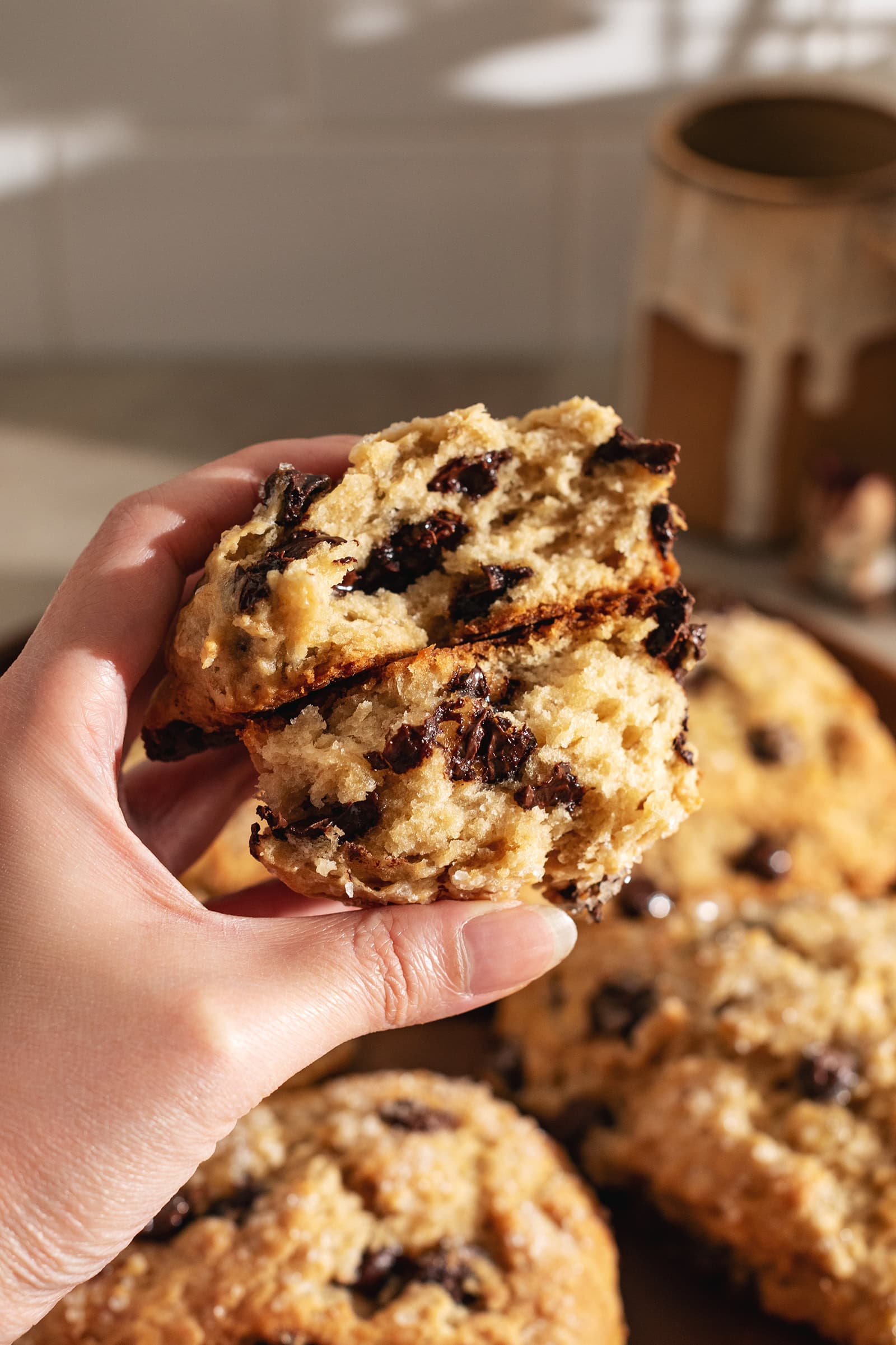 A hand holding two halves of a banana chocolate chip scone to show the texture and melted chocolate chips inside.