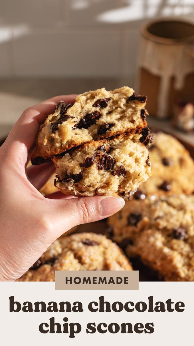 A hand holding two halves of a banana chocolate chip scone to show the texture and melted chocolate chips inside.