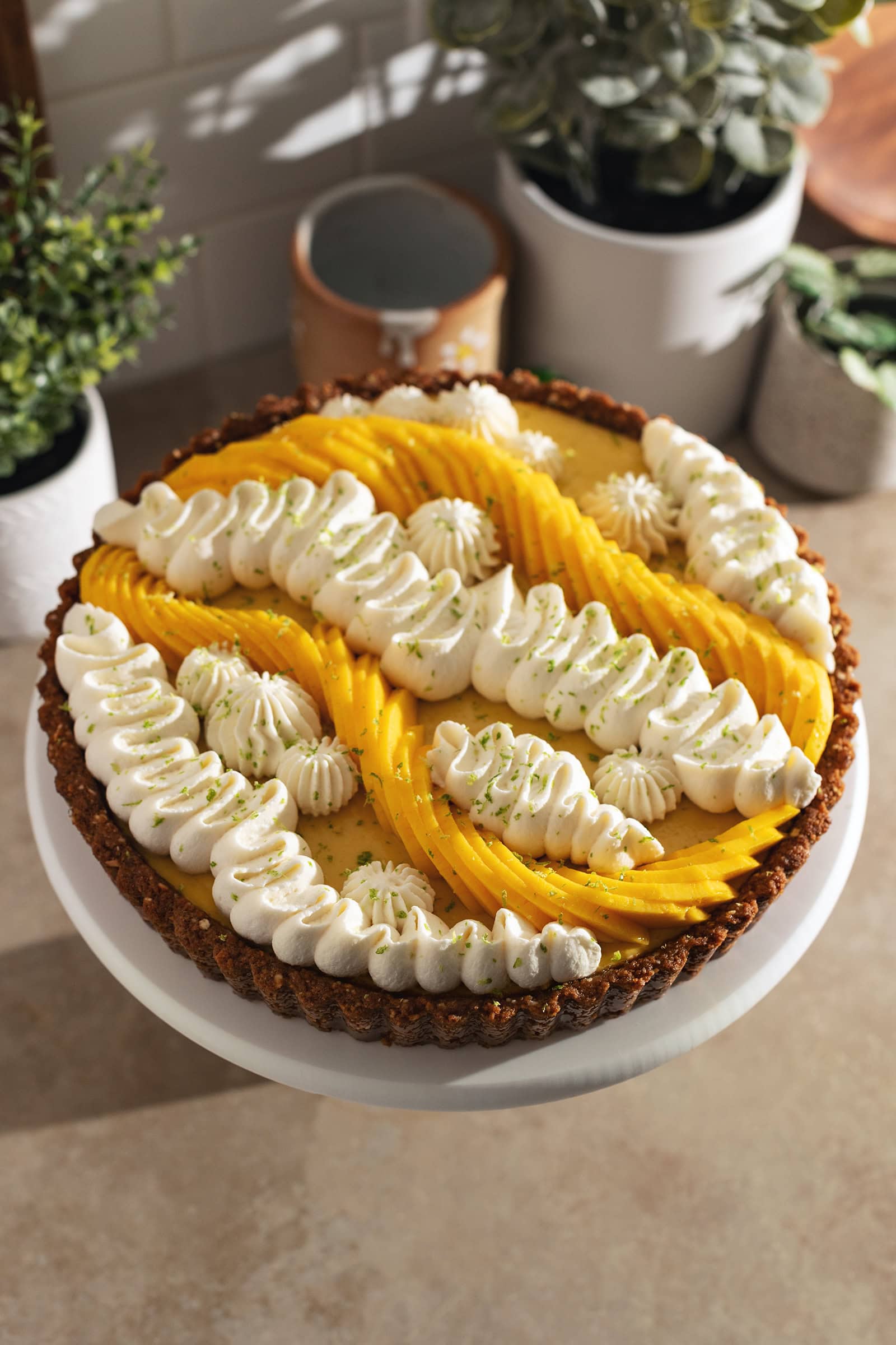A mango tart decorated with squiggles of whipped cream and fresh mangoes on a cake stand.