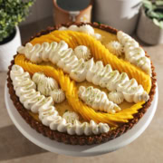 A mango tart decorated with squiggles of whipped cream and fresh mangoes on a cake stand.