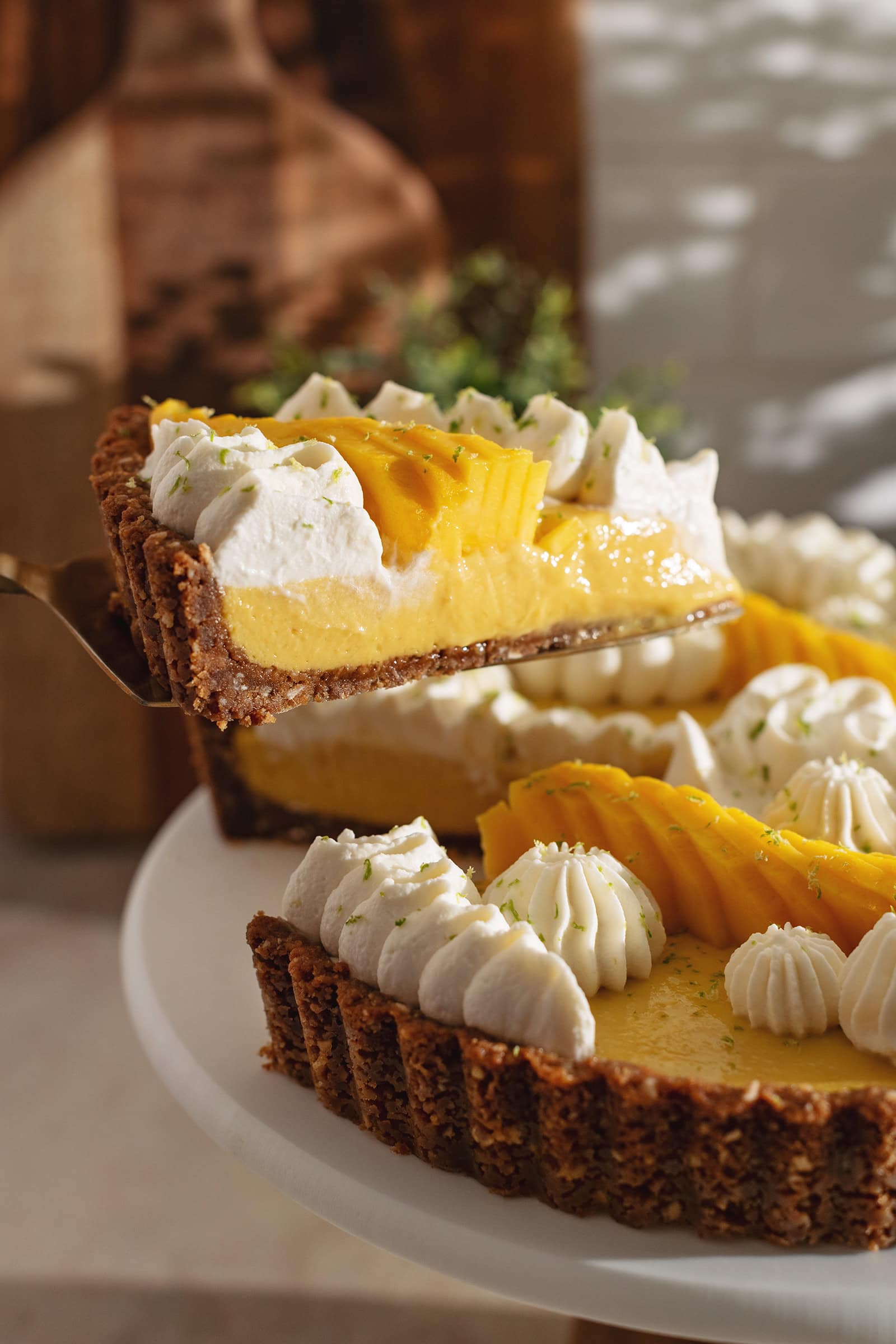 A slice of mango tart lifted from the rest of the tart with a cake server to show the cross-section view inside.
