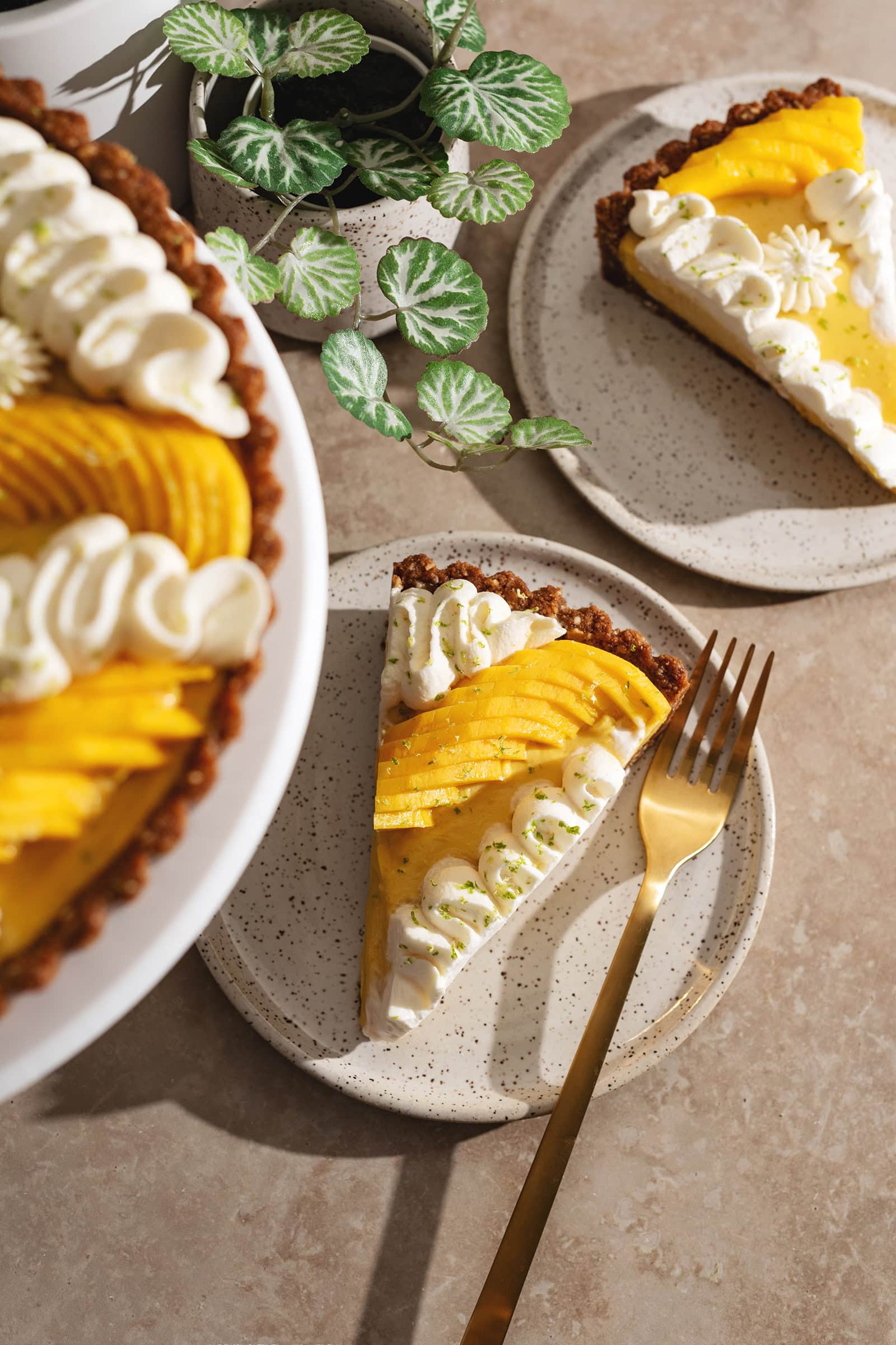 Two mango tart slices on plates with the rest of the tart blurred in the foreground.