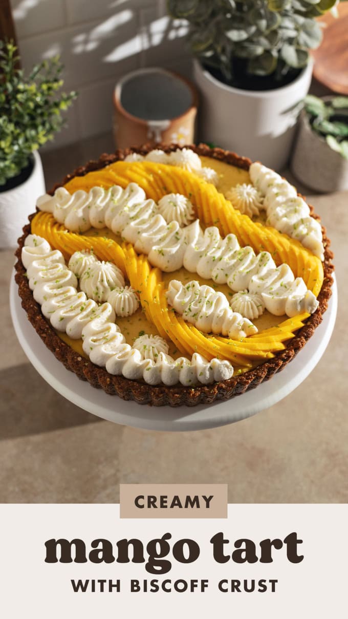 A mango tart decorated with squiggles of whipped cream and fresh mangoes on a cake stand.
