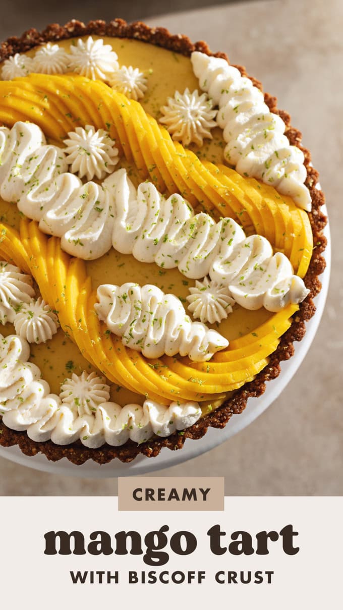 Close-up of a mango tart decorated with squiggles of whipped cream and fresh mangoes.